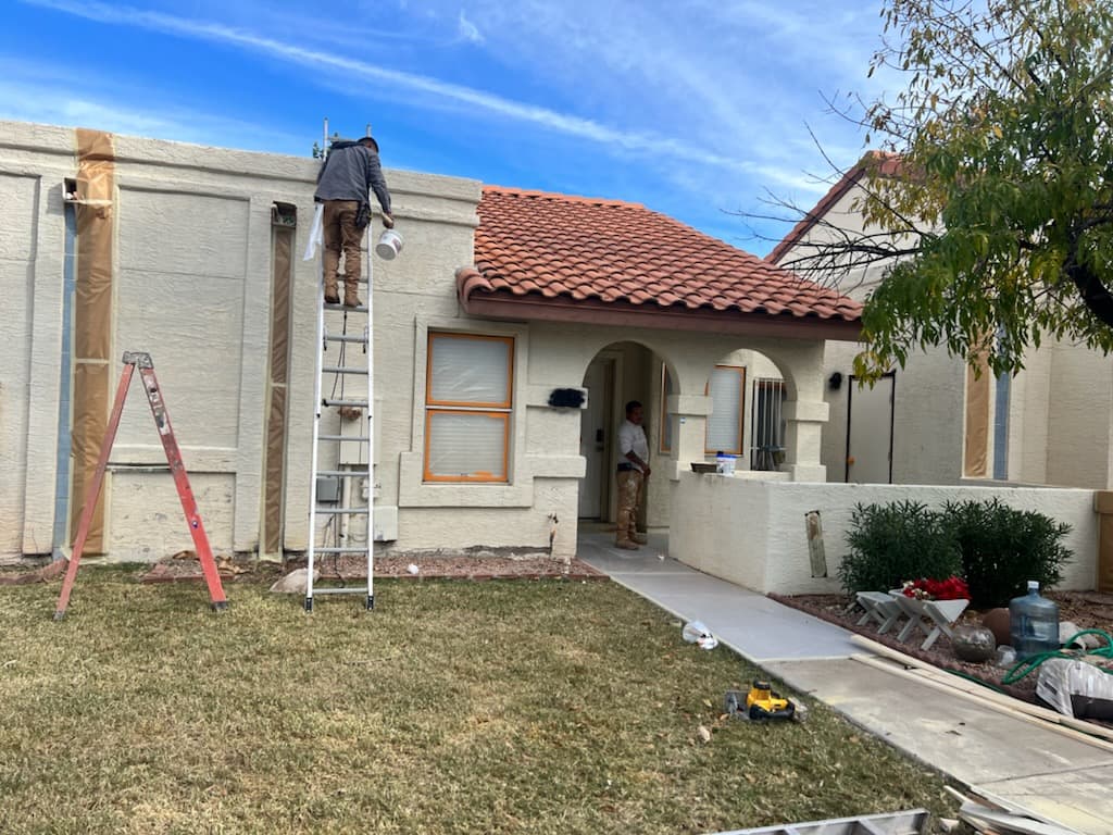 Painter on a ladder masking the fascia of a cream stucco home with a red tile roof