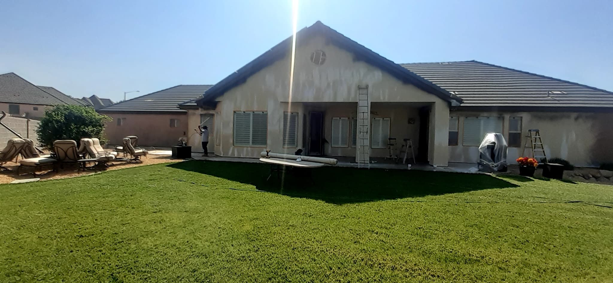 Rear of a home with windows masked off and a painter spraying the wall