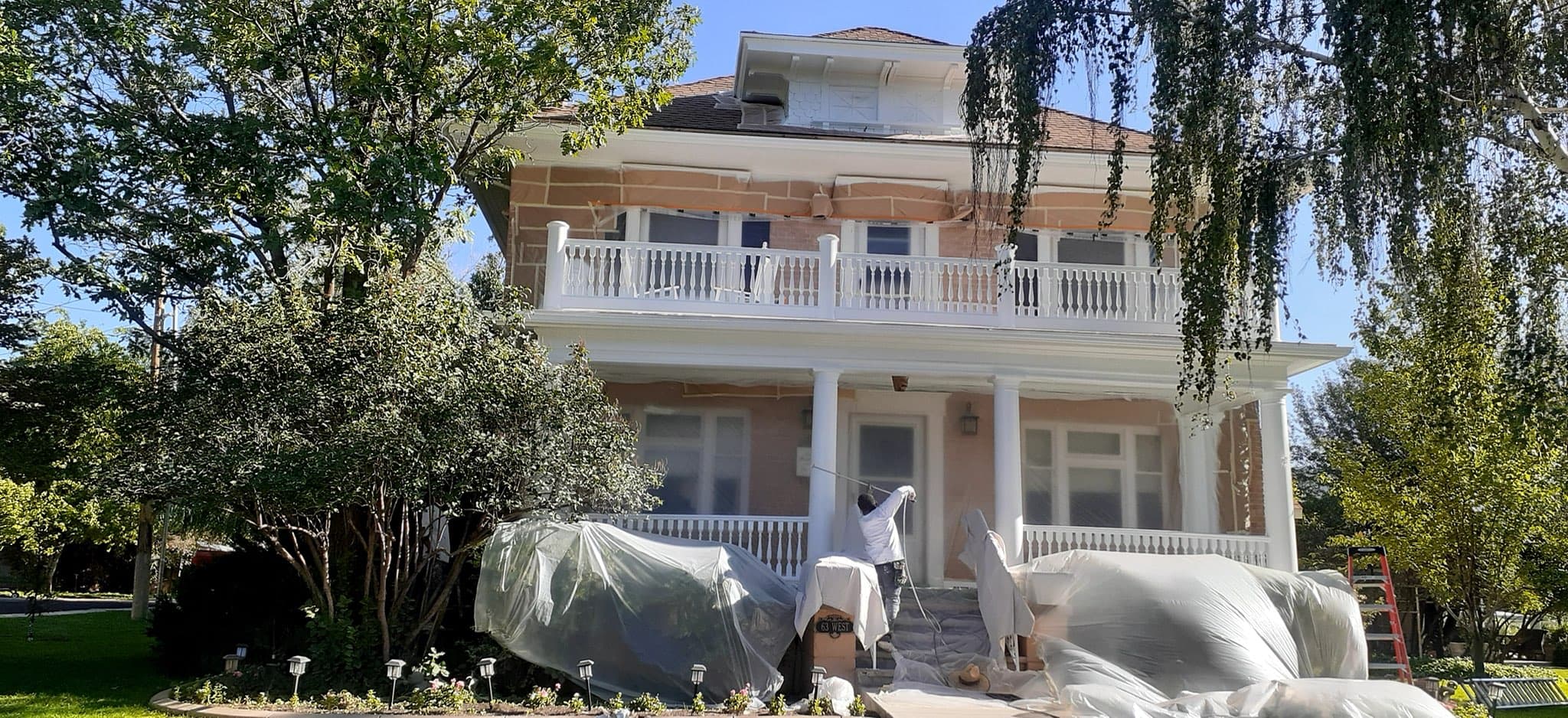 Historic two-story brick home draped in plastic sheeting during trim preparation