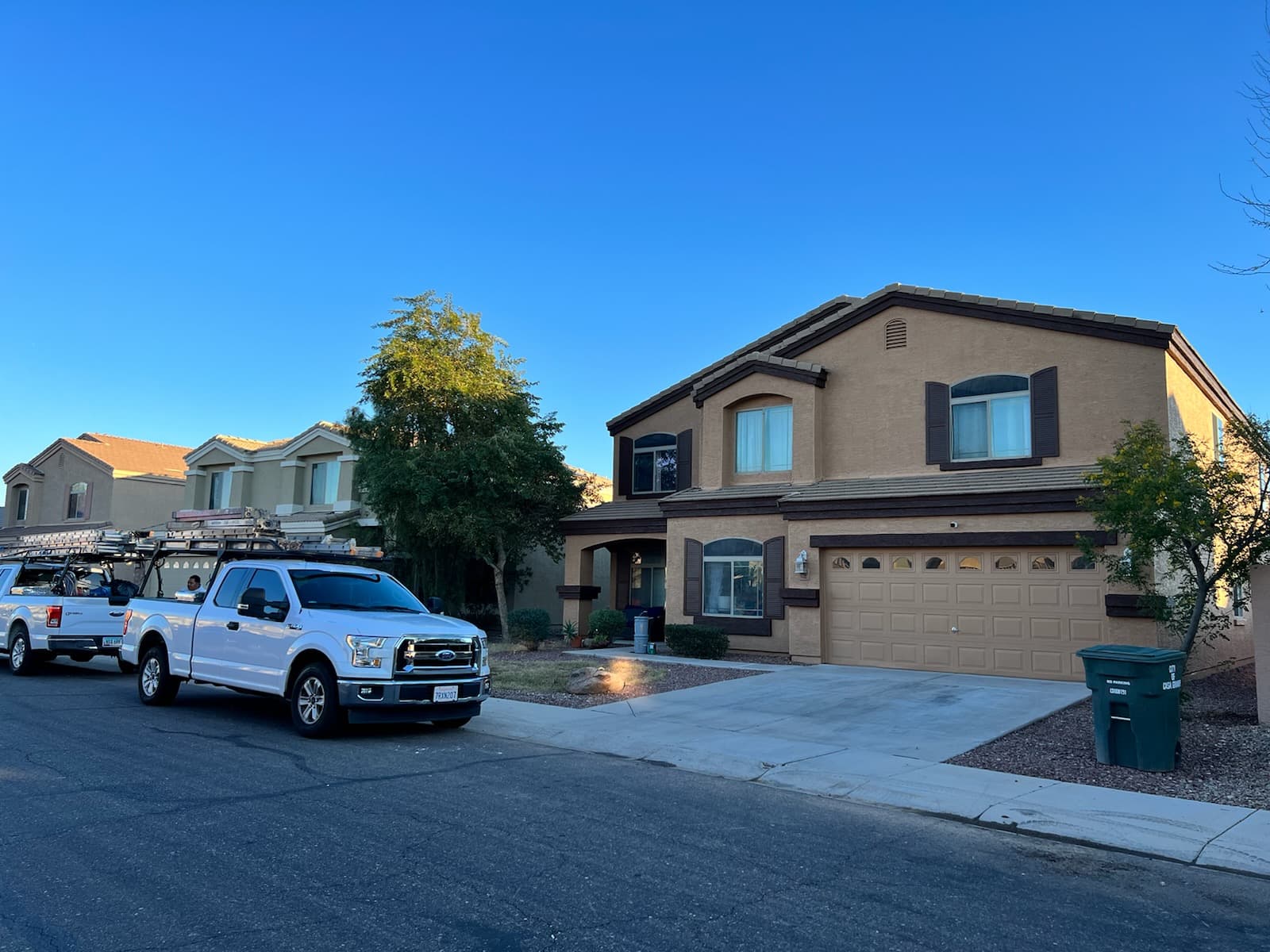 The same two-story home from the street with company trucks and ladders parked outside