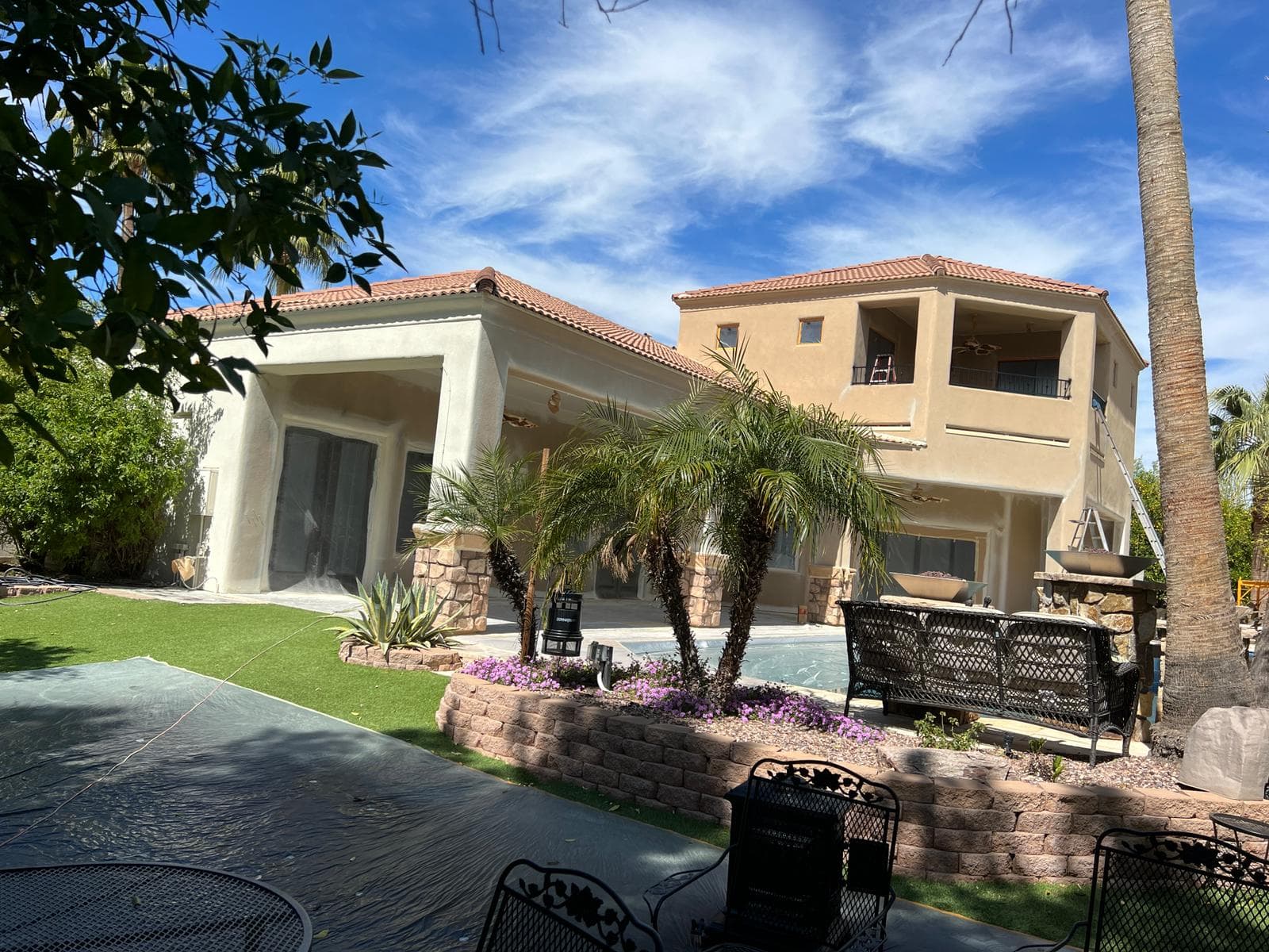 Large two-story home beside a pool with doors and windows masked for painting