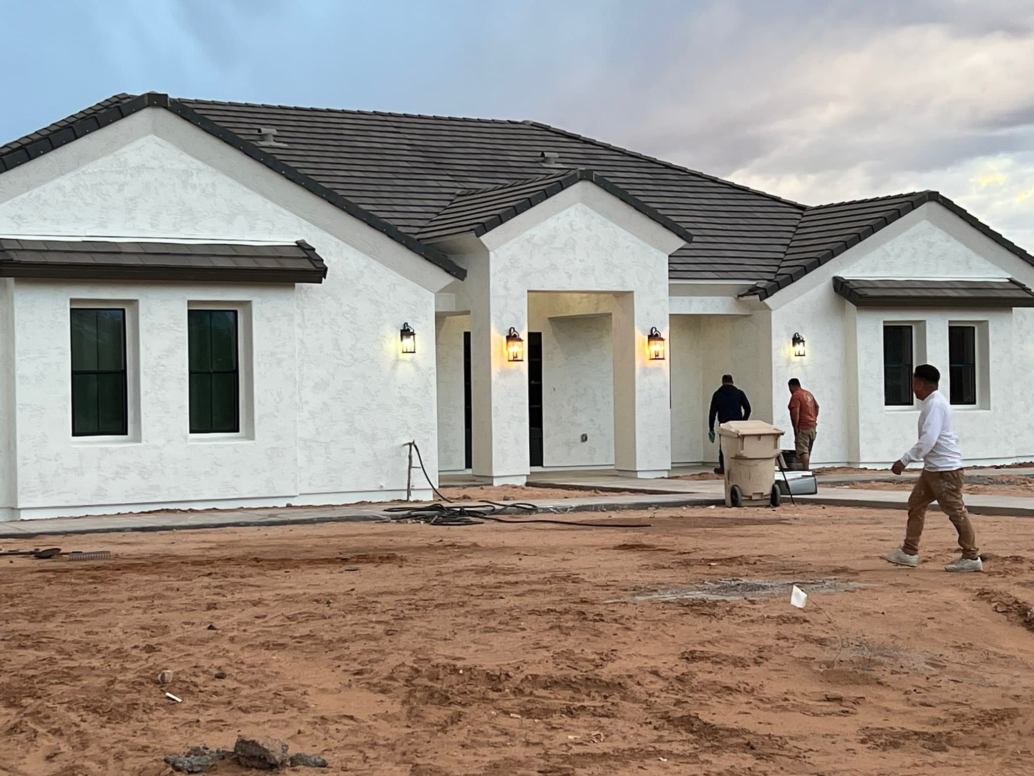Newly built white stucco home at dusk with the crew finishing up