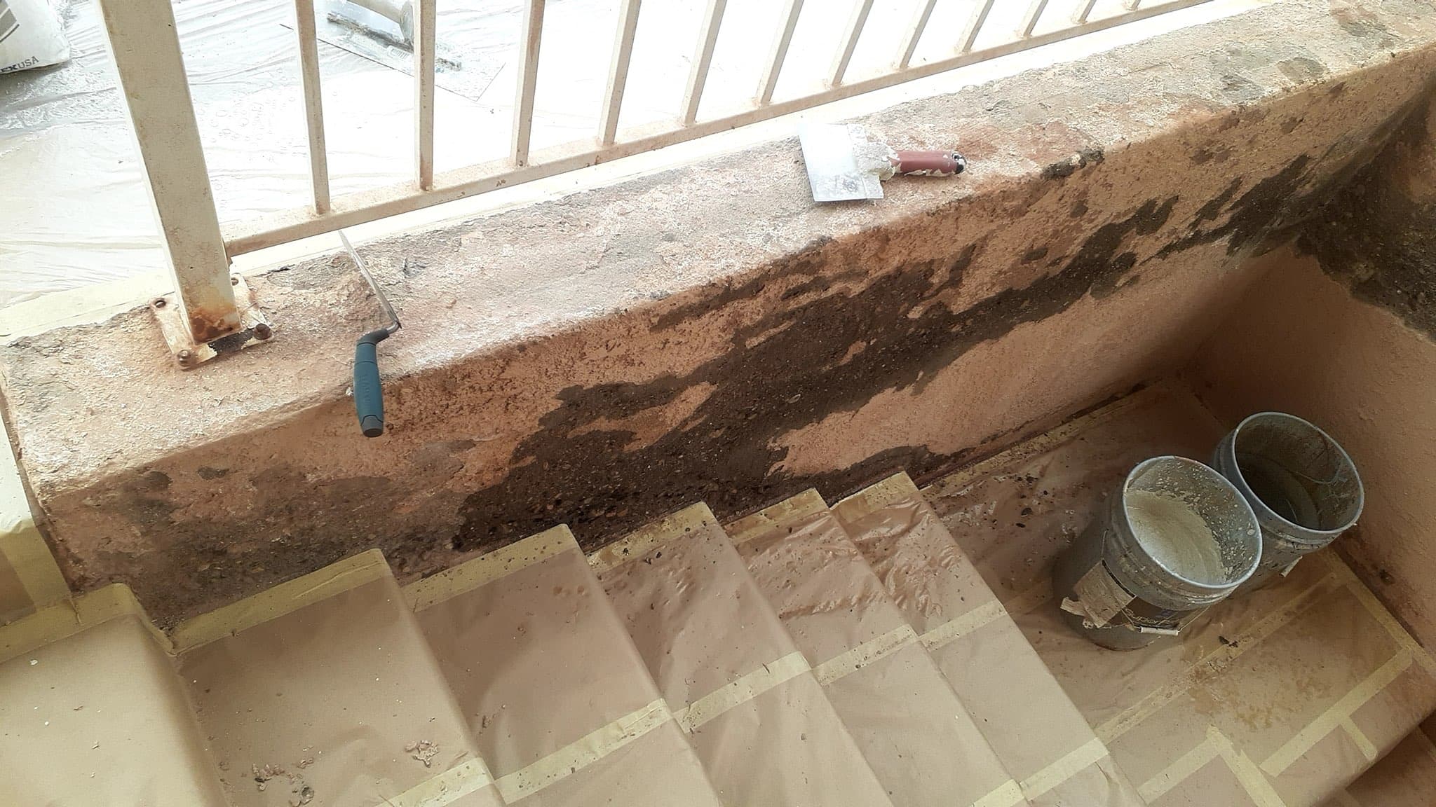 Stairwell wall with heavy water staining and damaged stucco, steps papered off